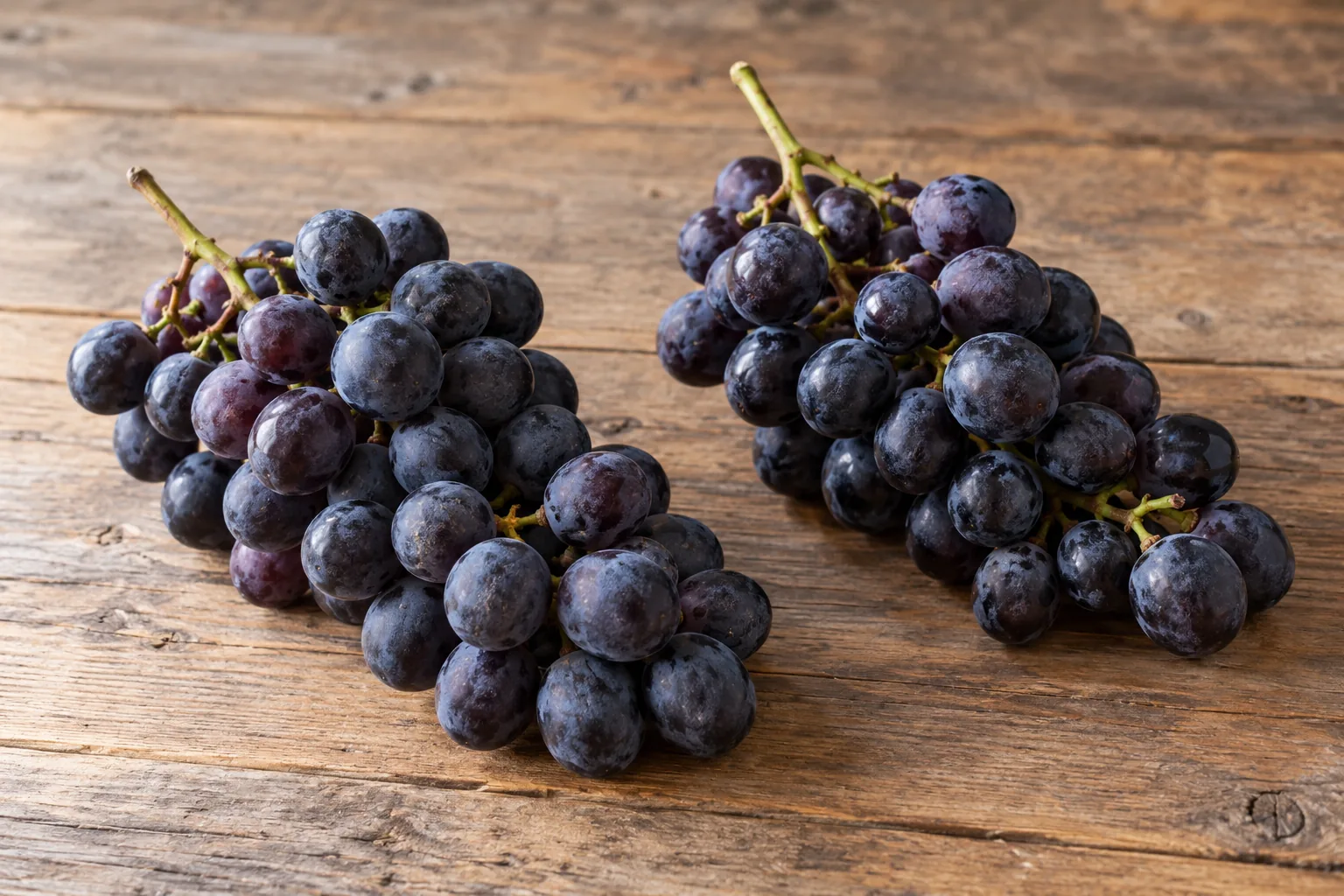 Two clusters of dark grapes on a wooden table, with no label and no printed text