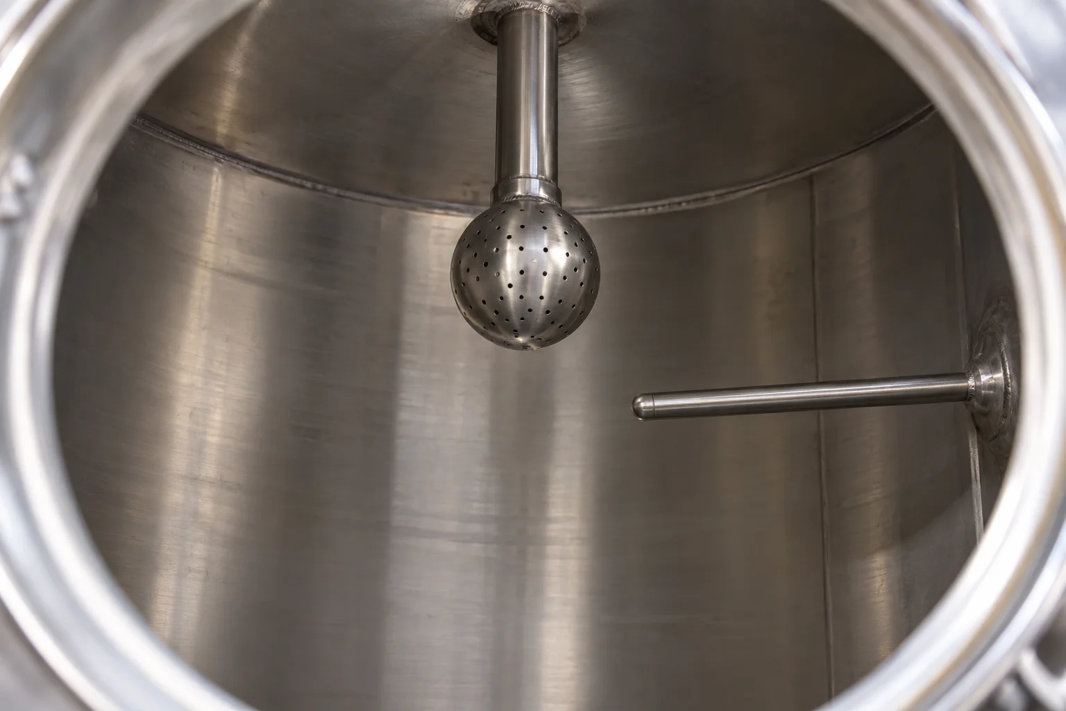 Perforated static spray ball suspended inside a stainless steel tank beside a projecting thermowell